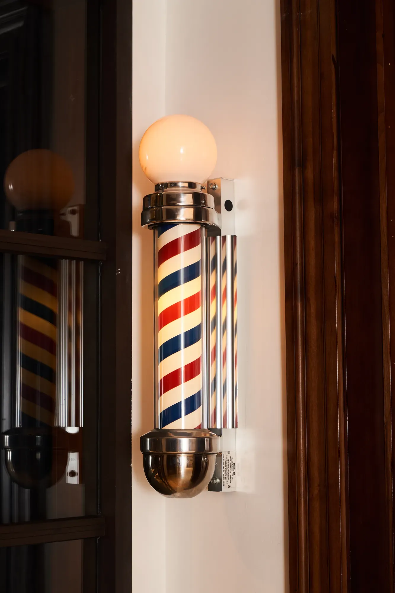 Illuminated vintage barber pole with red, white, and blue stripes mounted on the wall.