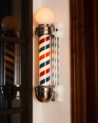 Illuminated vintage barber pole with red, white, and blue stripes mounted on the wall.