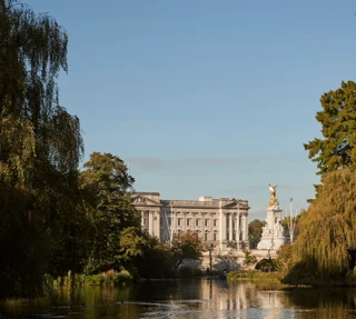 View across St James’s Park lake towards Buckingham Palace and Victoria Memorial, framed by trees in warm evening light.