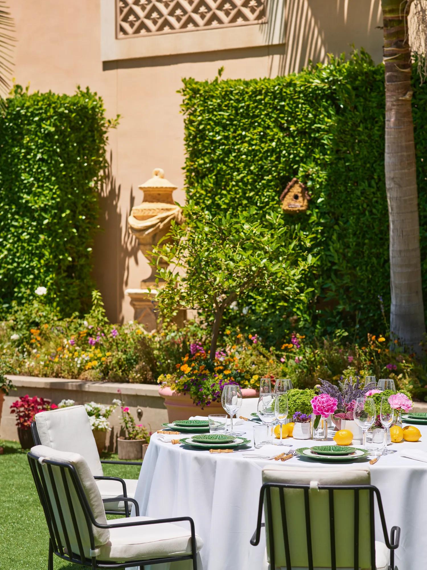 Close-up of a dressed reception table with green leaf-pattern plates, lemons and pink-purple florals against hedges on the Garden Terrace.