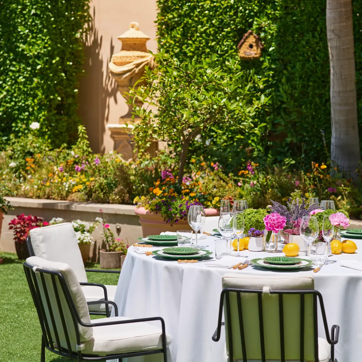 Close-up of a dressed reception table with green leaf-pattern plates, lemons and pink-purple florals against hedges on the Garden Terrace.