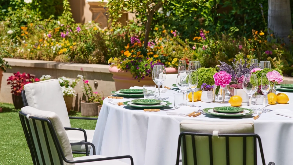 Close-up of a dressed reception table with green leaf-pattern plates, lemons and pink-purple florals against hedges on the Garden Terrace.