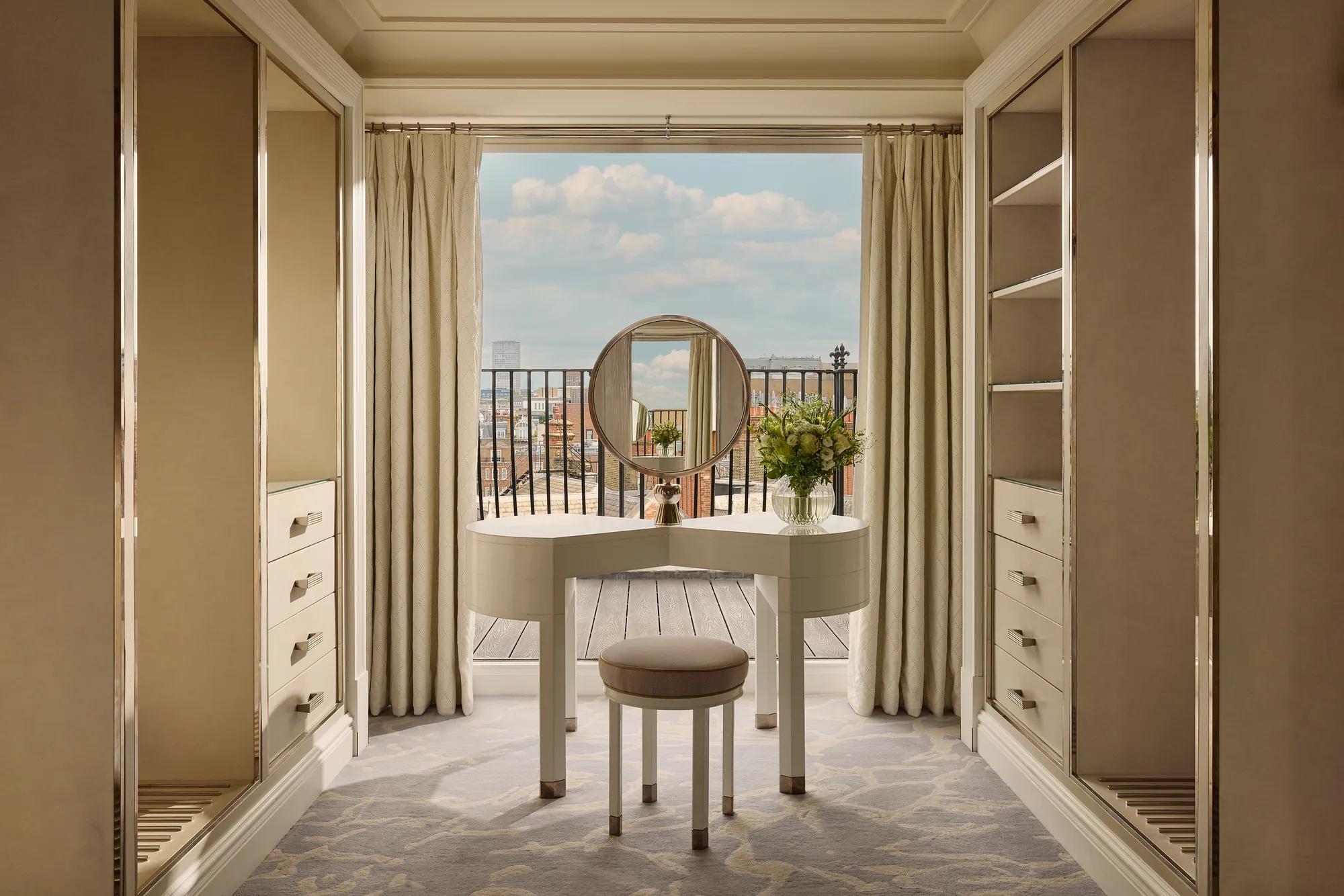 Elegant dressing area with vanity table, round mirror, open wardrobes, and balcony view.