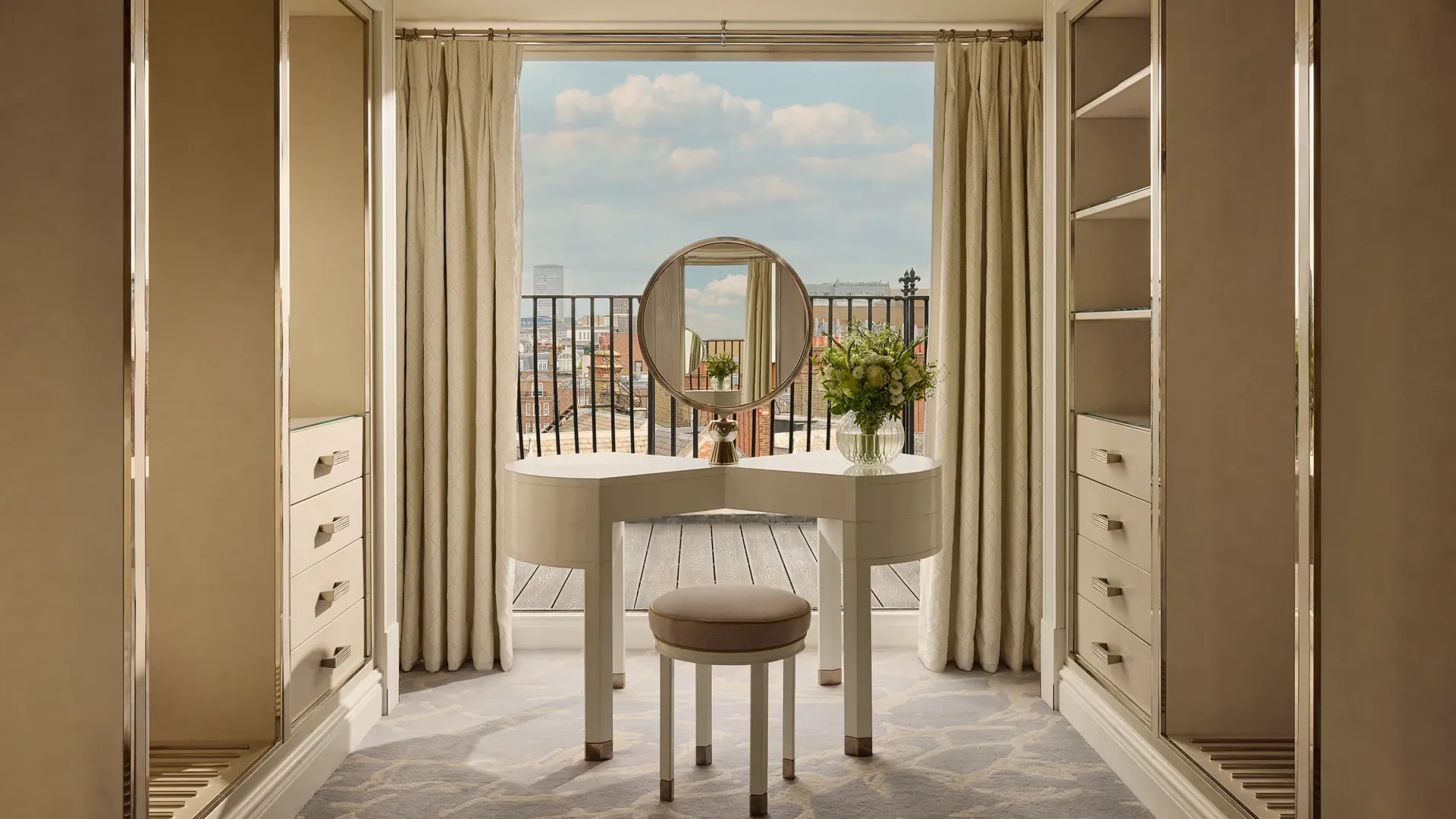 Elegant dressing area with vanity table, round mirror, open wardrobes, and balcony view.
