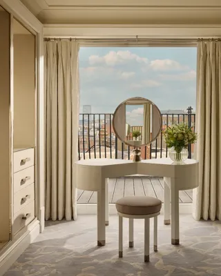Elegant dressing area with vanity table, round mirror, open wardrobes, and balcony view.