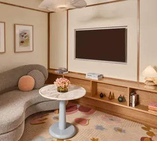 Cosy sitting area with curved sofa, marble-topped table, wall-mounted TV, built-in wooden shelving, and framed artwork.