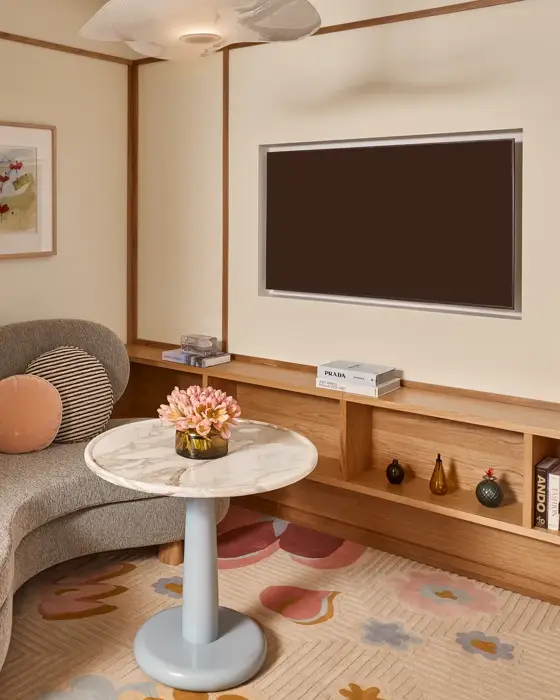 Cosy sitting area with curved sofa, marble-topped table, wall-mounted TV, built-in wooden shelving, and framed artwork.
