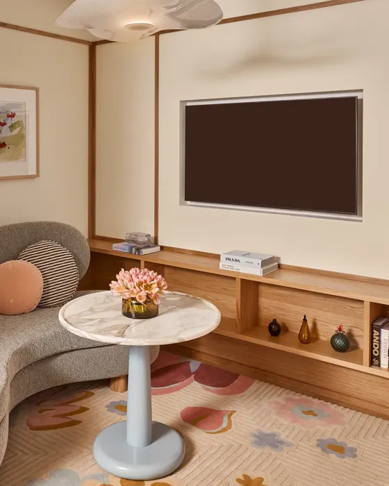 Cosy sitting area with curved sofa, marble-topped table, wall-mounted TV, built-in wooden shelving, and framed artwork.