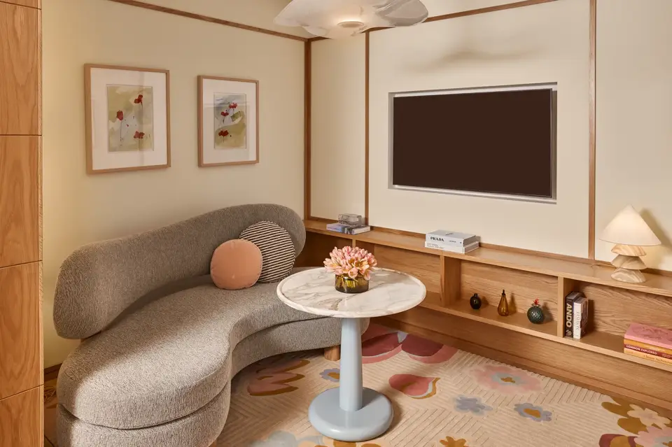 Cosy sitting area with curved sofa, marble-topped table, wall-mounted TV, built-in wooden shelving, and framed artwork.