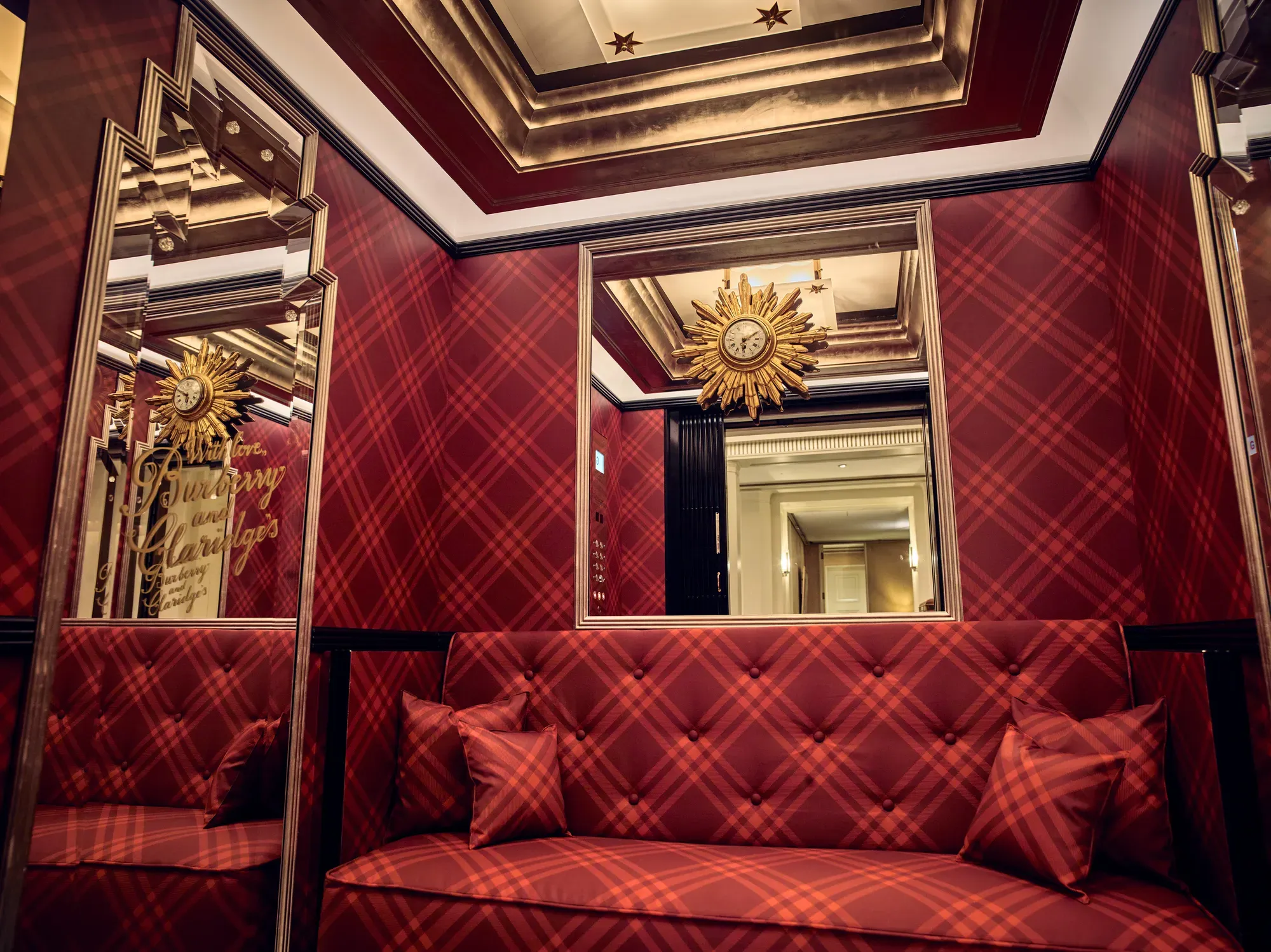 Red tartan upholstered seating with mirrored panels and decorative sunburst clock in an elegant, richly detailed interior