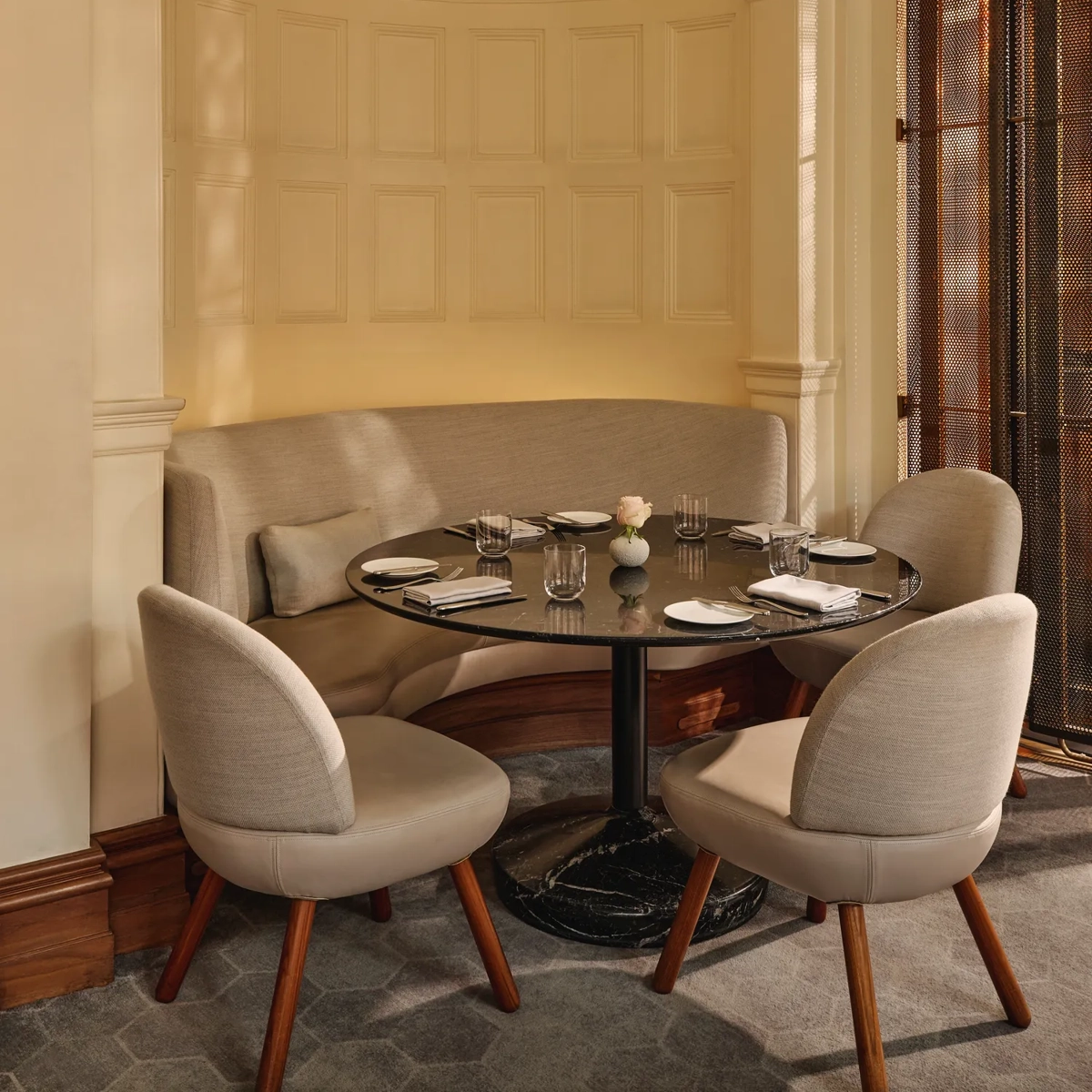 Small dining nook with a curved upholstered banquette, round black table, and soft beige chairs beneath an ornate domed ceiling.