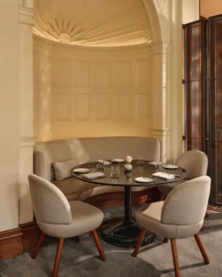 Small dining nook with a curved upholstered banquette, round black table, and soft beige chairs beneath an ornate domed ceiling.