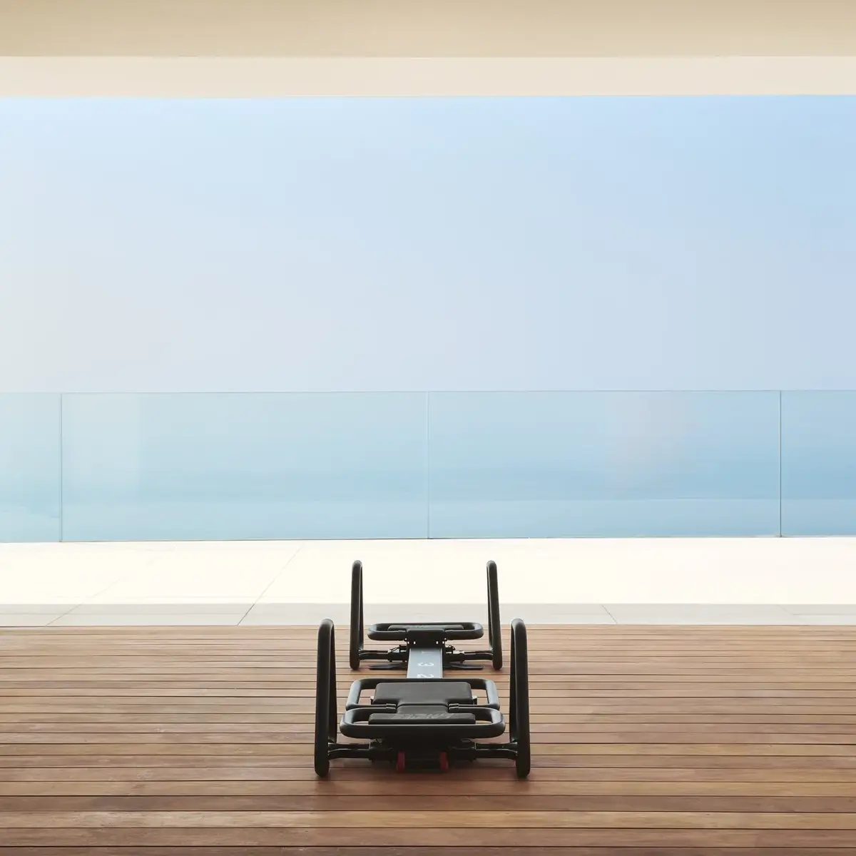 Pilates reformer on a wooden terrace overlooking the sea through floor-to-ceiling glass.
