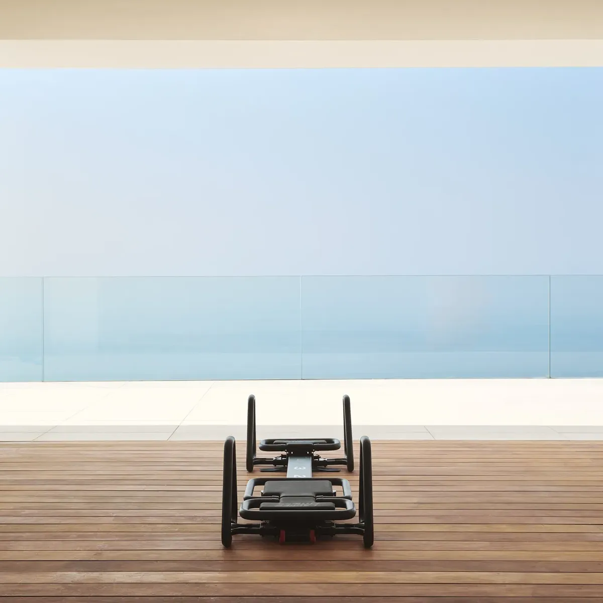 Pilates reformer on a wooden terrace overlooking the sea through floor-to-ceiling glass.