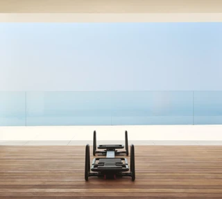 Pilates reformer on a wooden terrace overlooking the sea through floor-to-ceiling glass.