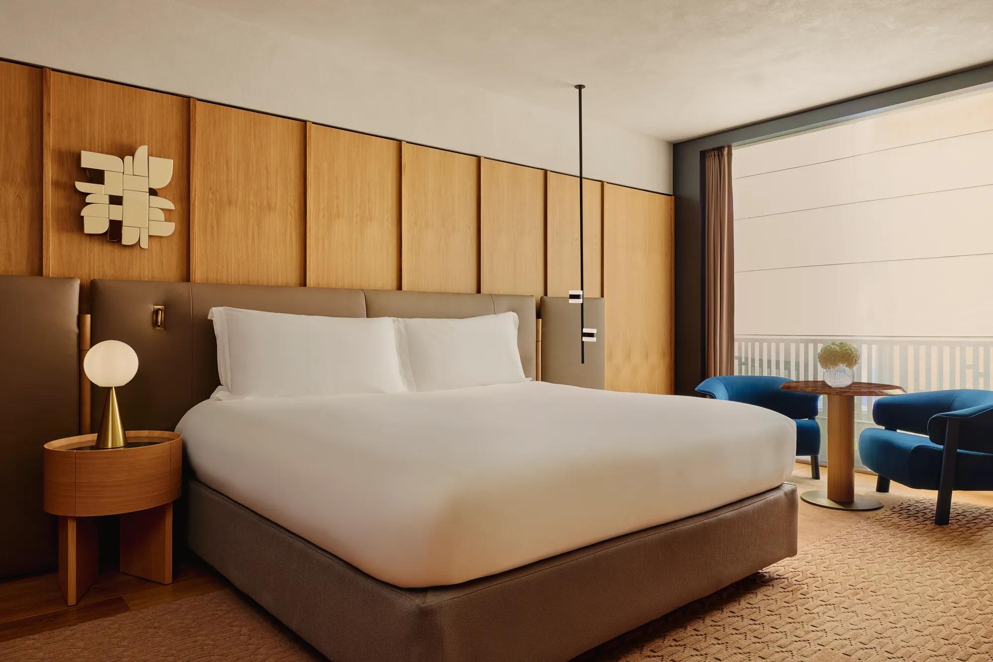King bed with upholstered headboard and wood-panelled wall, beside a seating area with balcony views.