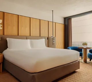 King bed with upholstered headboard and wood-panelled wall, beside a seating area with balcony views.