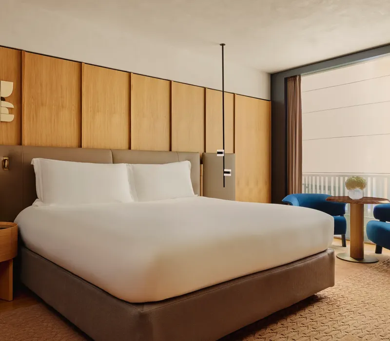 King bed with upholstered headboard and wood-panelled wall, beside a seating area with balcony views.