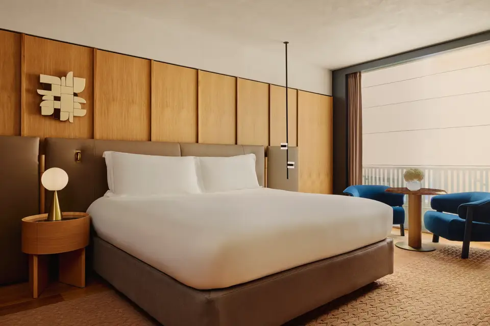 King bed with upholstered headboard and wood-panelled wall, beside a seating area with balcony views.