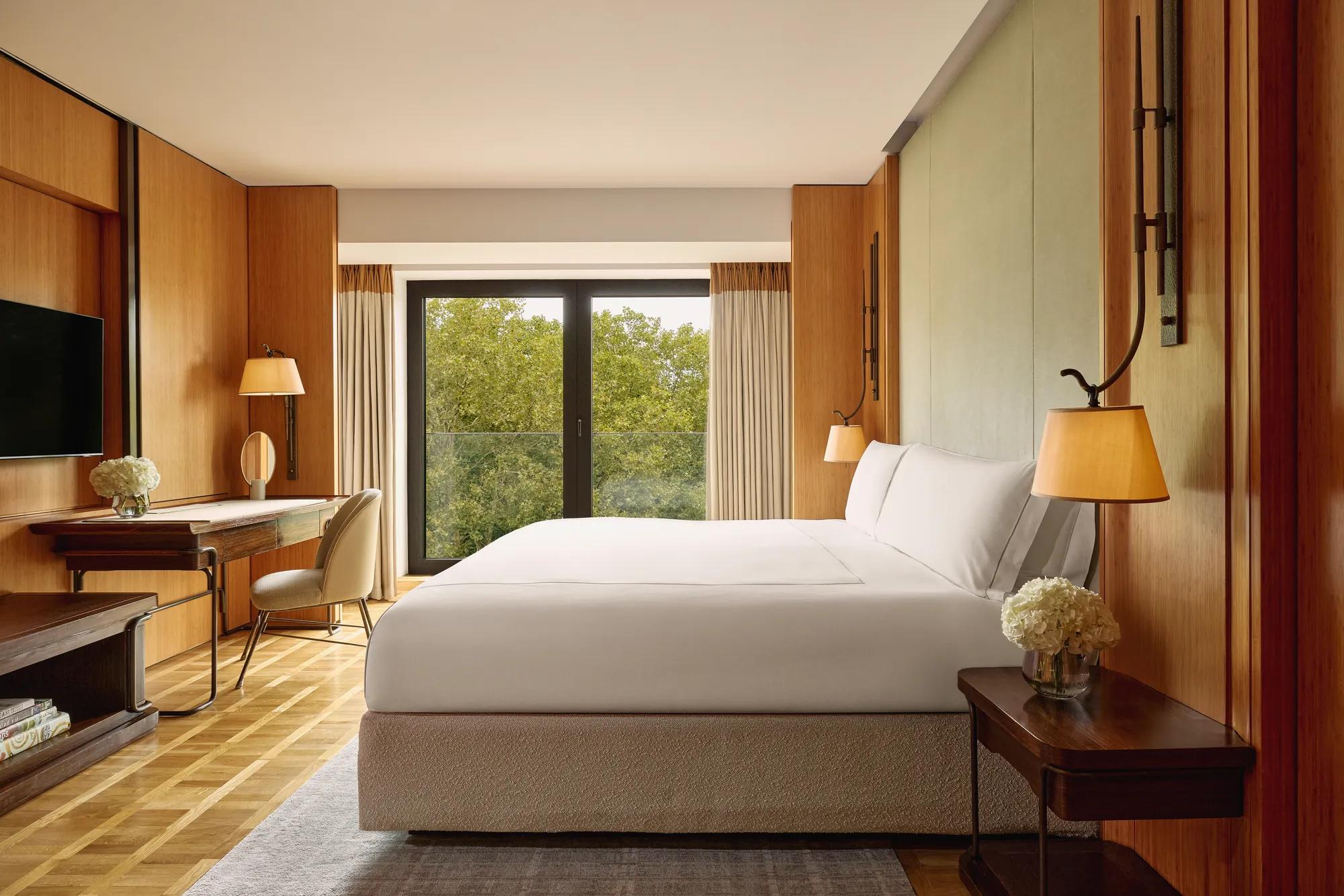 Opus Suite bedroom with king bed, writing desk, and floor-to-ceiling windows overlooking trees.