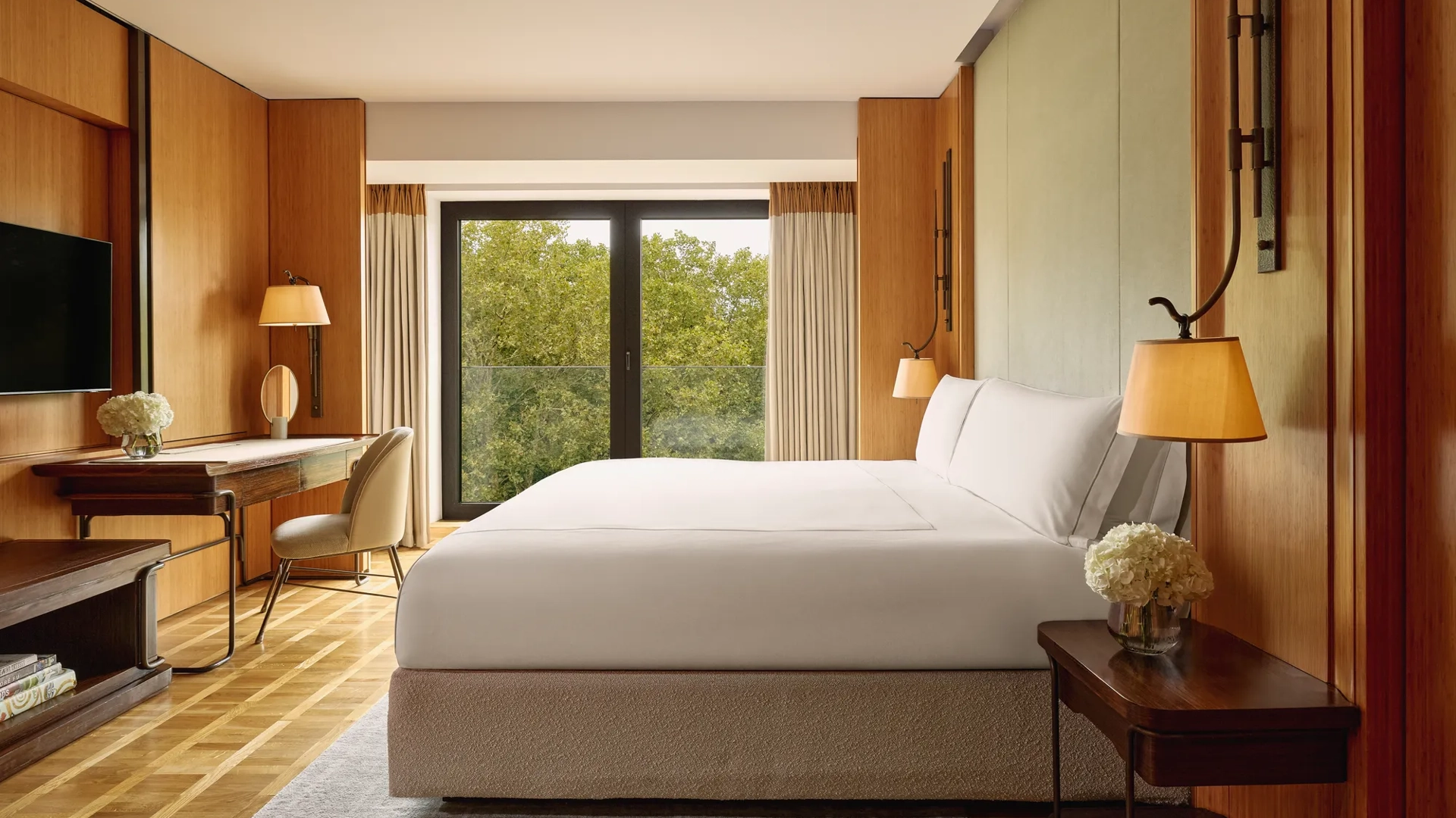 Opus Suite bedroom with king bed, writing desk, and floor-to-ceiling windows overlooking trees.