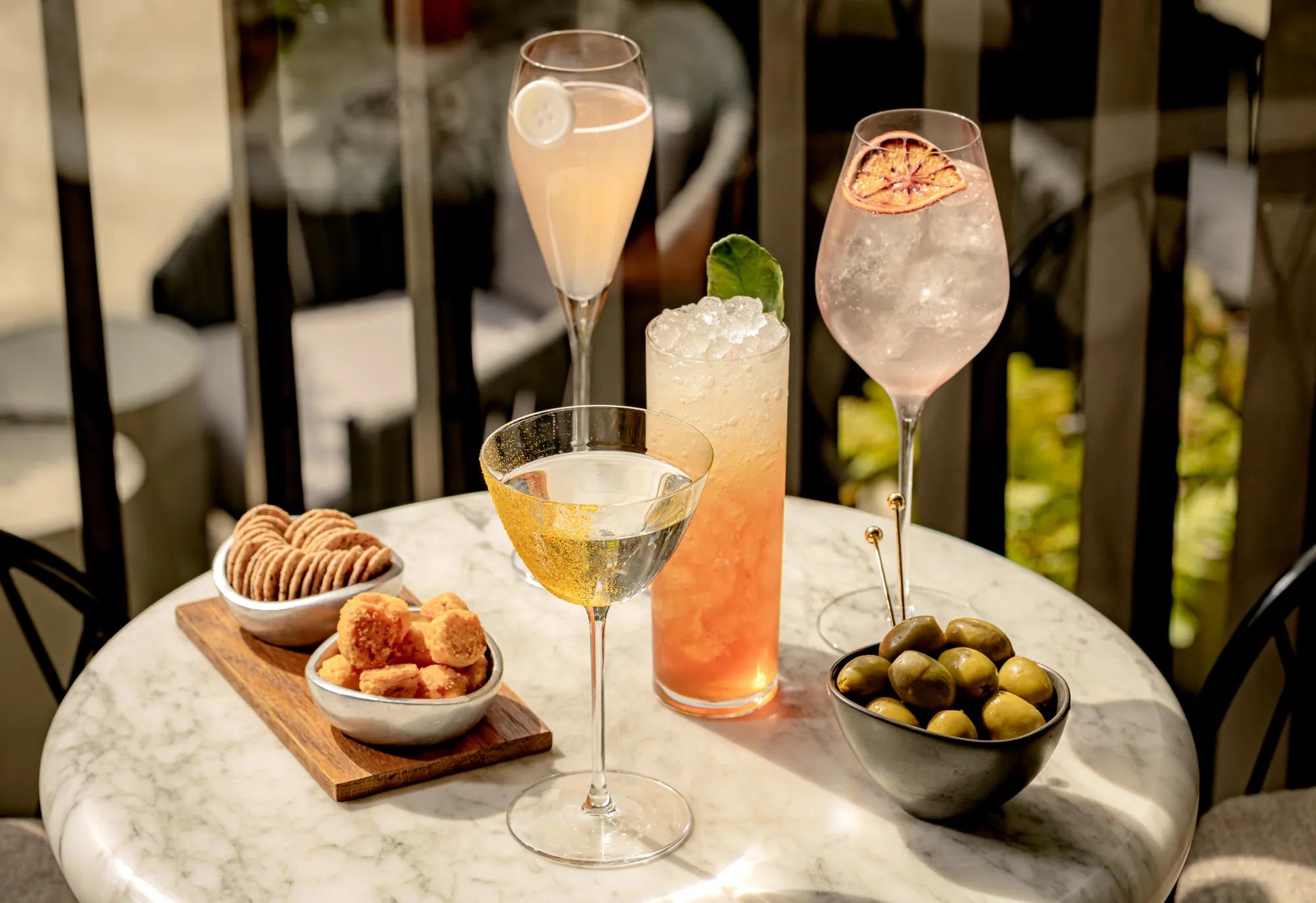 A table of four cocktails, olives and snacks
