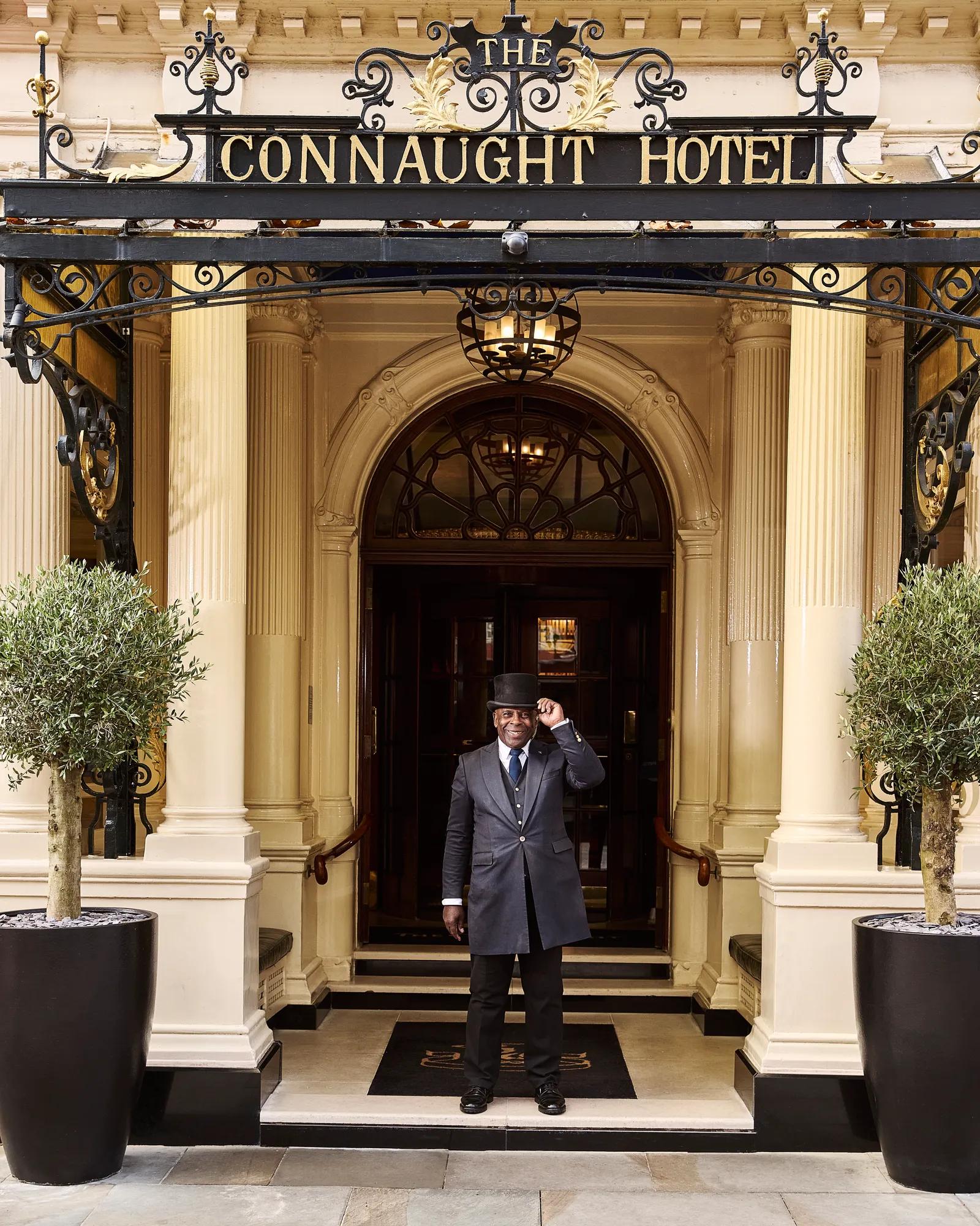 Doorman standing at The Connaught Hotel entrance beneath ornate black canopy.