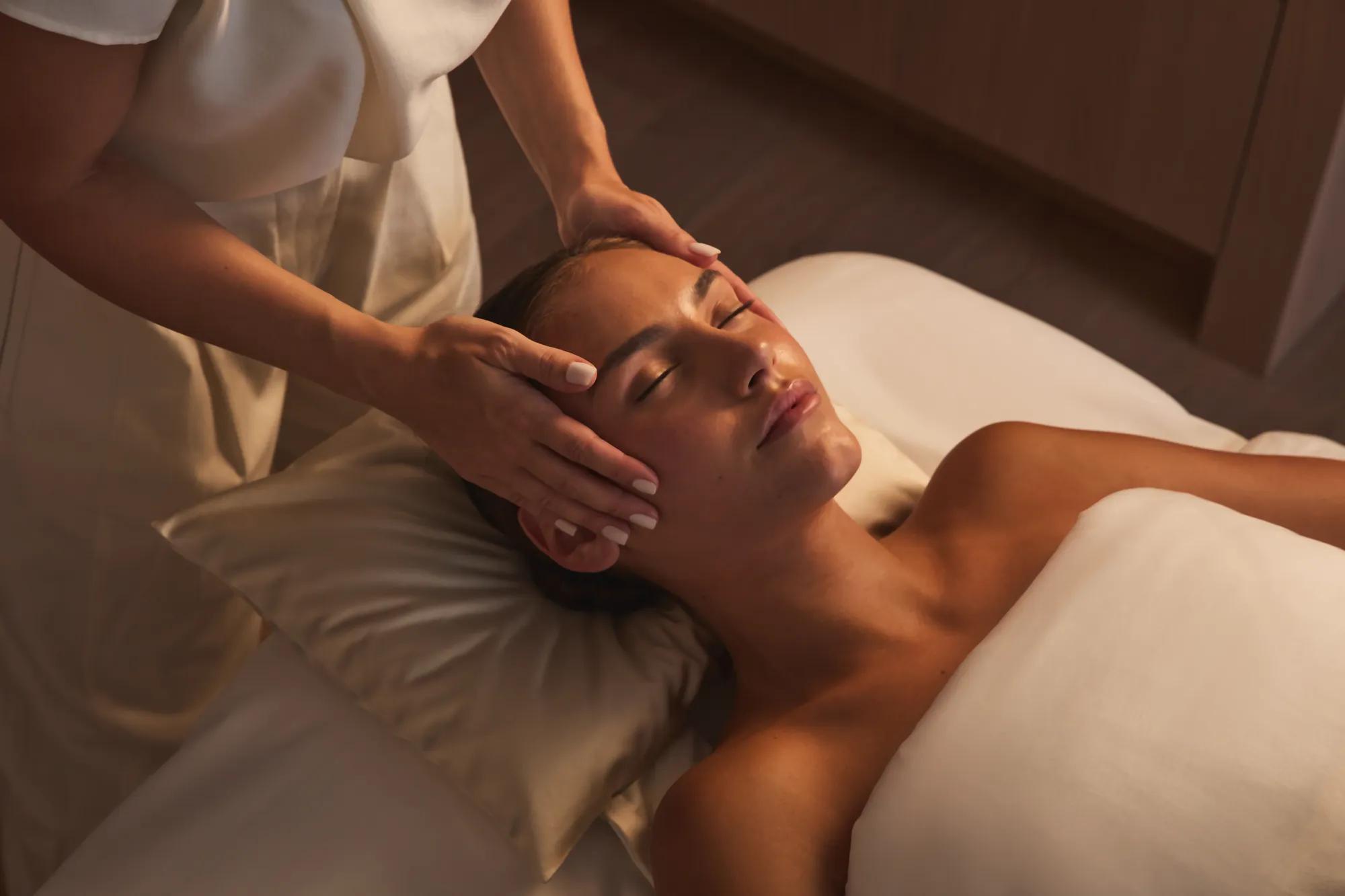 Praticienne massant délicatement les tempes d’une cliente lors d’un soin du visage relaxant.