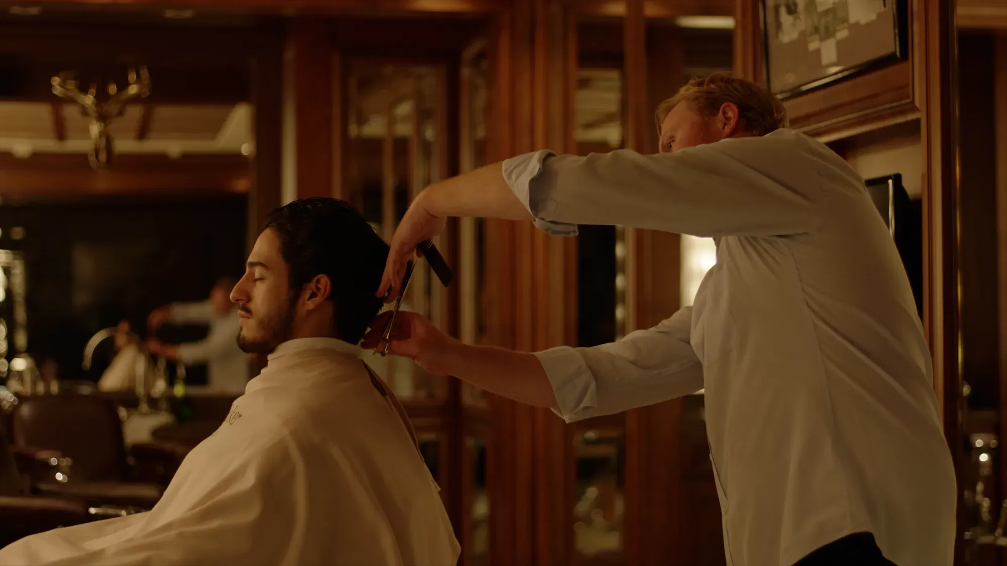 Barber trimming a client’s hair with comb and scissors in classic wood-paneled barbershop.