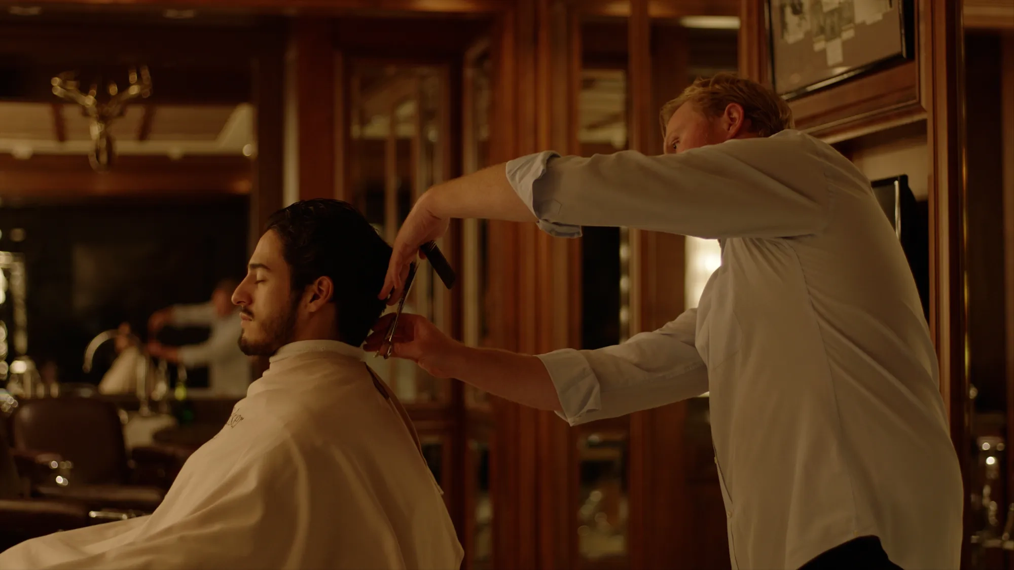 Barber trimming a client’s hair with comb and scissors in classic wood-paneled barbershop.