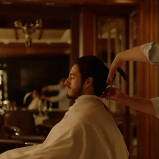 Barber trimming a client’s hair with comb and scissors in classic wood-paneled barbershop.