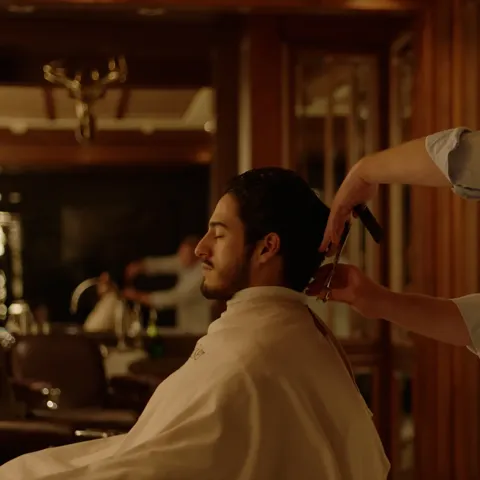 Barber trimming a client’s hair with comb and scissors in classic wood-paneled barbershop.