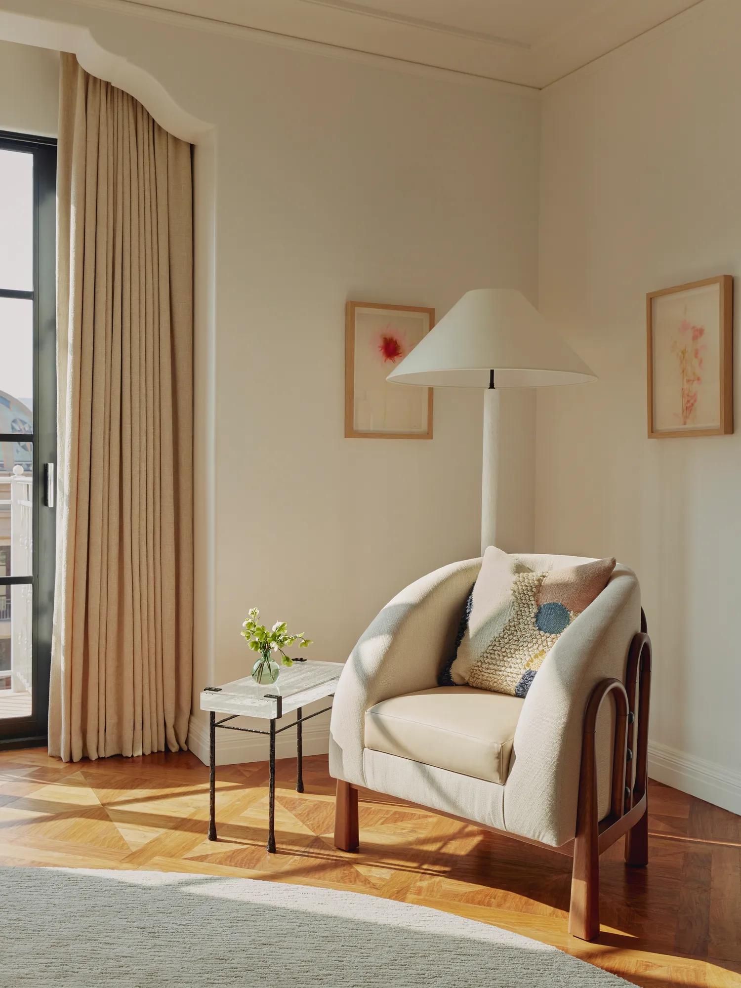 Corner reading nook with a cream armchair, textured cushion, marble-topped side table with a small vase of flowers, and framed botanical prints on the wall.