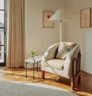 Corner reading nook with a cream armchair, textured cushion, marble-topped side table with a small vase of flowers, and framed botanical prints on the wall.