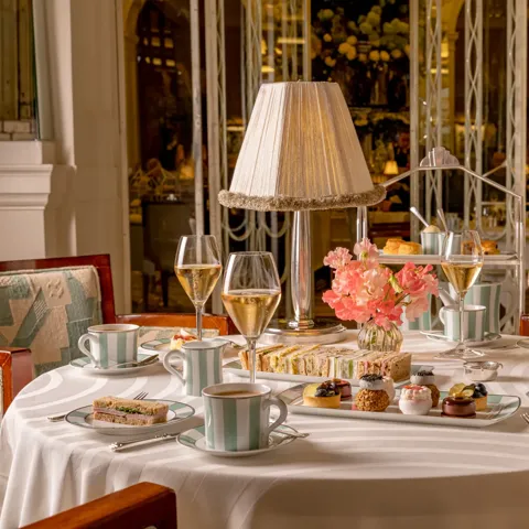 Afternoon tea table with champagne, sandwiches and pastries around a lamp centrepiece in an elegant restaurant.