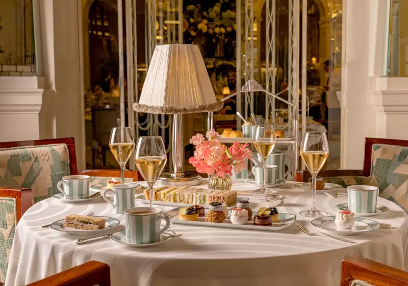 Afternoon tea table with champagne, sandwiches and pastries around a lamp centrepiece in an elegant restaurant.