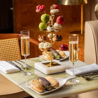 Tiered stand of pastries with champagne flutes and savoury eclairs on marble table.