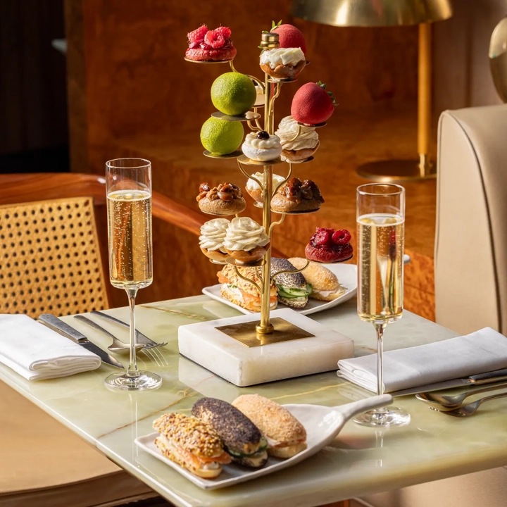 Tiered stand of pastries with champagne flutes and savoury eclairs on marble table.