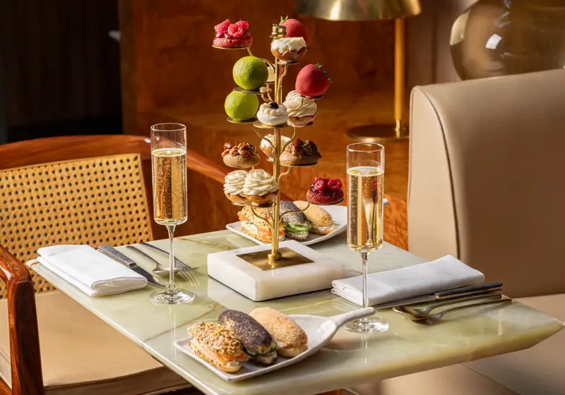 Tiered stand of pastries with champagne flutes and savoury eclairs on marble table.