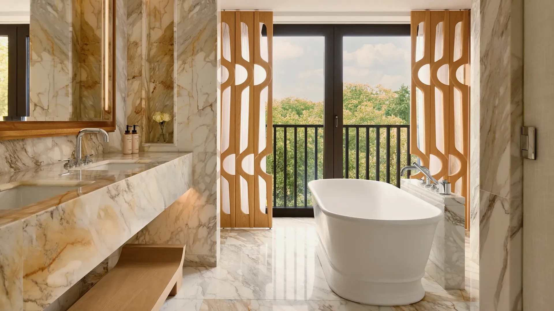 Marble bathroom with freestanding bathtub, dual sinks, and large windows with leafy park views