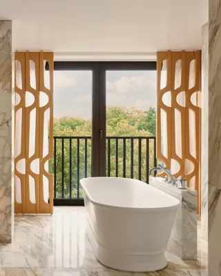 Marble bathroom with freestanding bathtub, dual sinks, and large windows with leafy park views