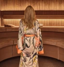 Person wearing patterned robe walking barefoot through a wooden spa interior with curved seating.