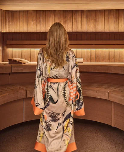 Person wearing patterned robe walking barefoot through a wooden spa interior with curved seating.