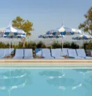 The Maybourne Beverly Hills ninth floor rooftop pool with blue loungers and striped umbrellas reflected in the water.