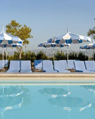 The Maybourne Beverly Hills ninth floor rooftop pool with blue loungers and striped umbrellas reflected in the water.