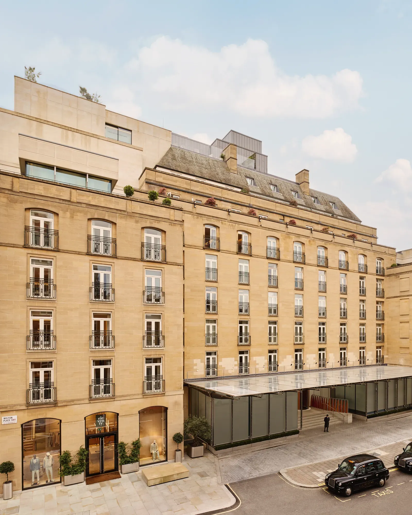 Exterior view of The Emory hotel with a stone façade, rows of balconies, and a glass entrance canopy on a city street.