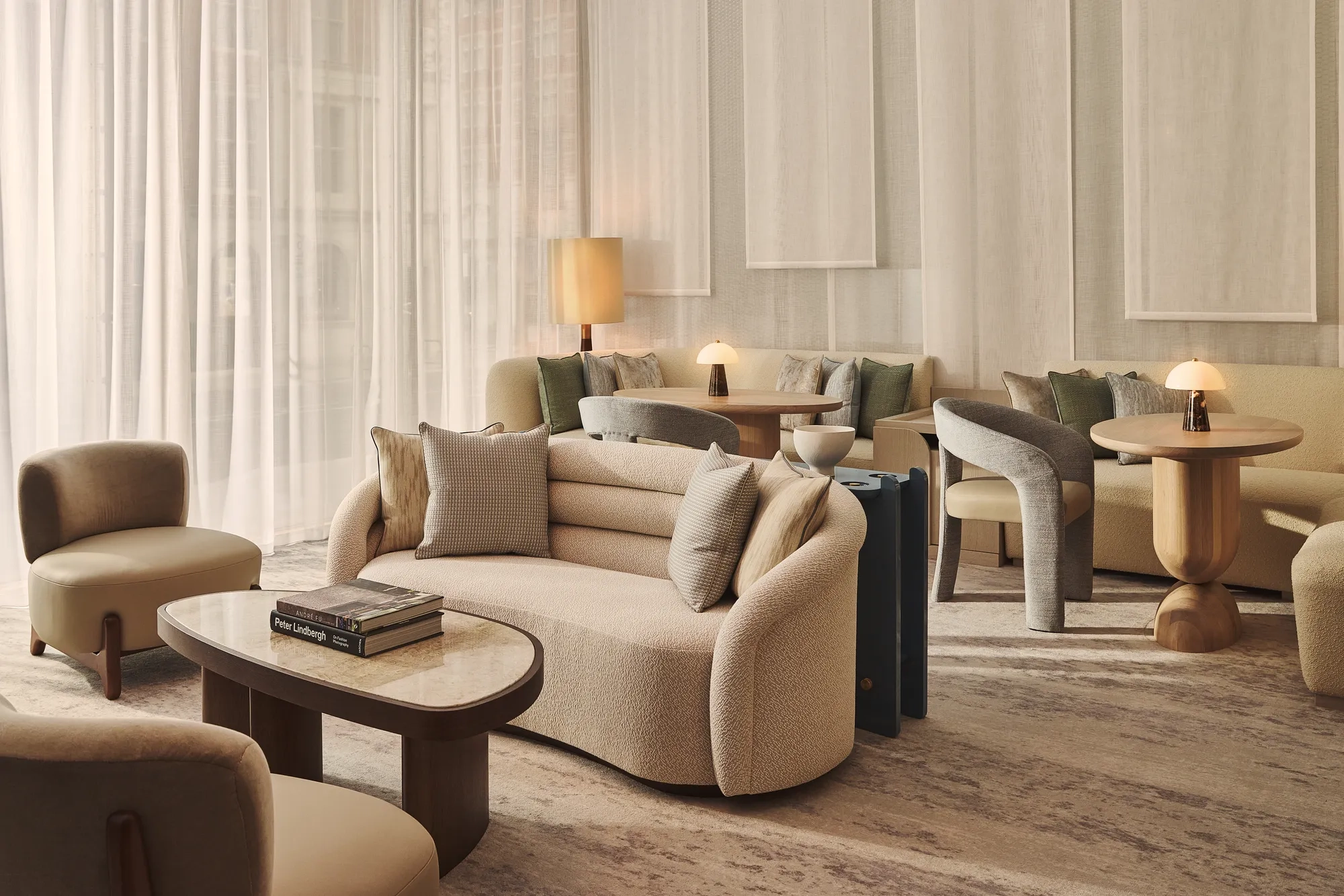 Serene lounge with soft beige seating, curved sofas and armchairs, warm table lamps and layered sheer curtains creating a calm, elegant setting.