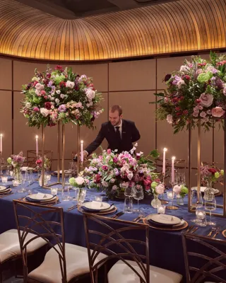 Private dining room with navy tablecloth, tall floral centerpieces, candles, and server pouring wine.