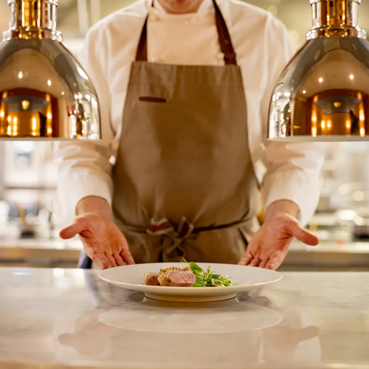 Chef presenting a plated dish under warm kitchen lights.