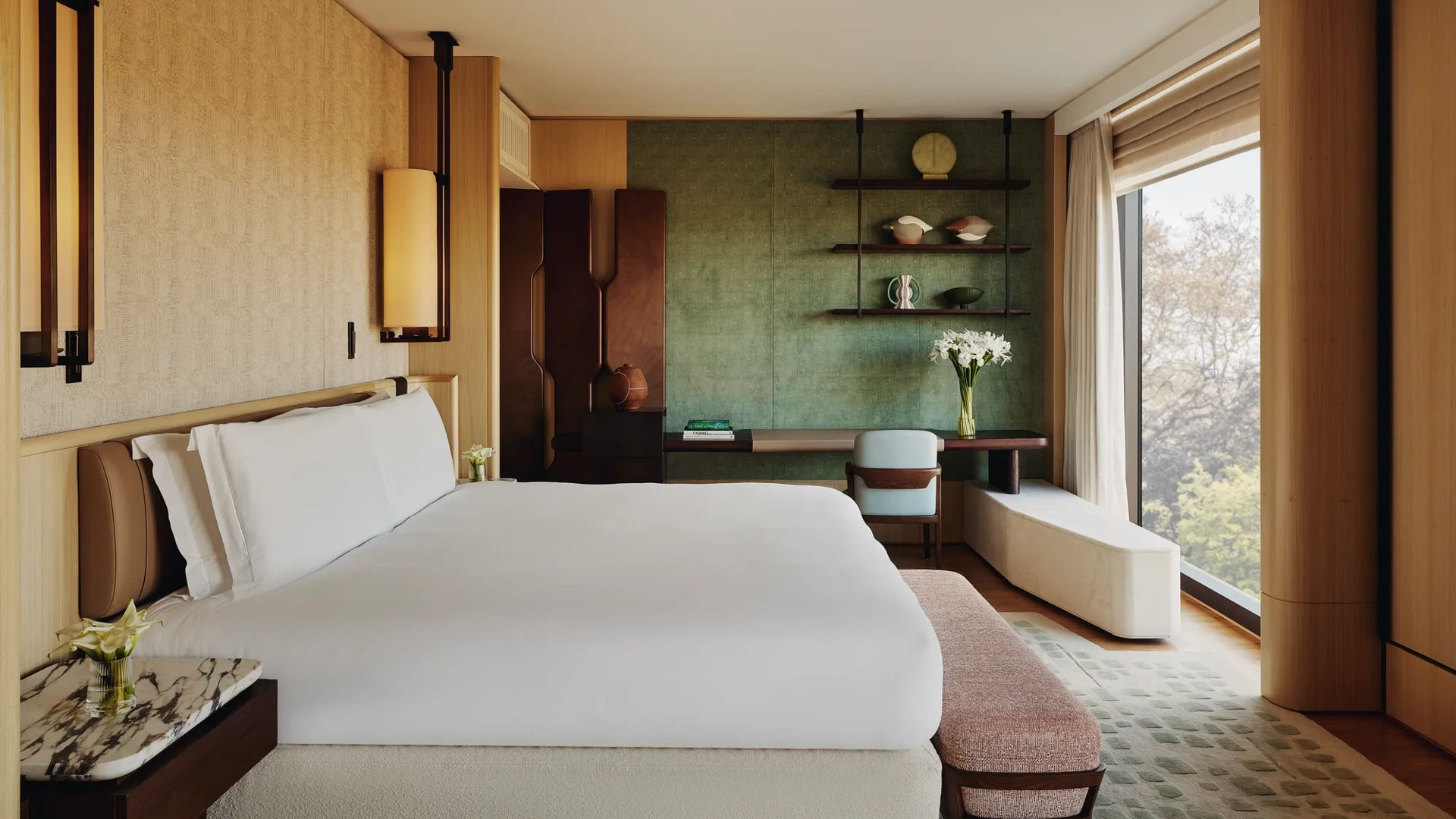 Contemporary bedroom with king bed, green feature wall, bespoke shelving, and park view through floor-to-ceiling window.